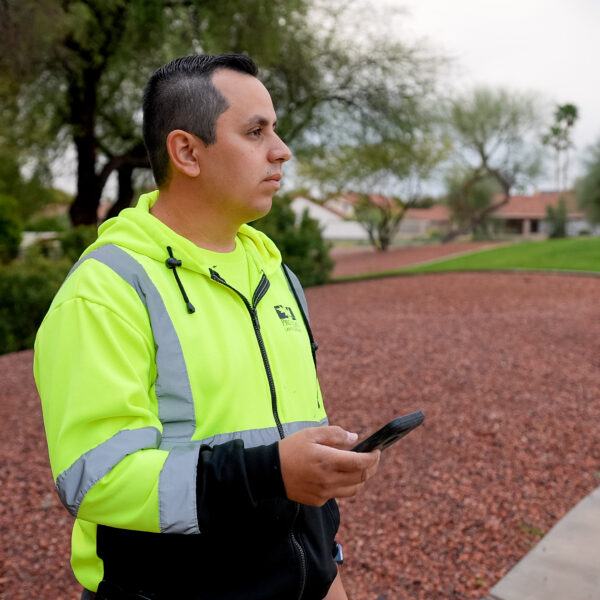 Technician on a property looking at the landscape while he holds his cell phone to control the sprinkler system